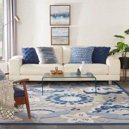 Blue-and-cream floral rug on floor with a cream sofa, glass coffee table, wooden chair, plant and abstract framed art
