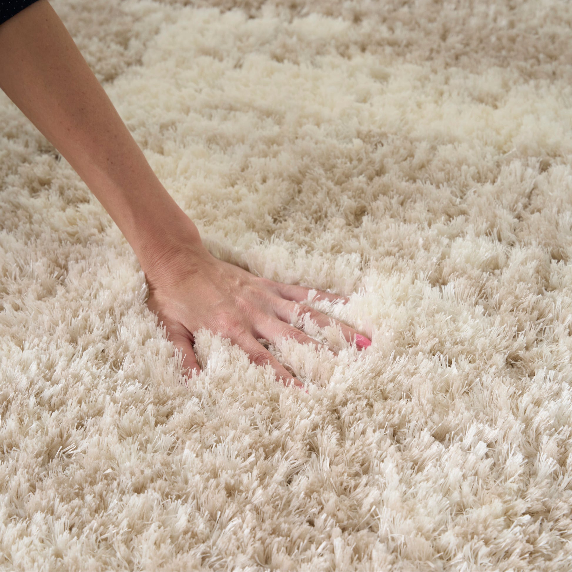 Cream shag rug with a hand pressing into the fluffy plush pile.