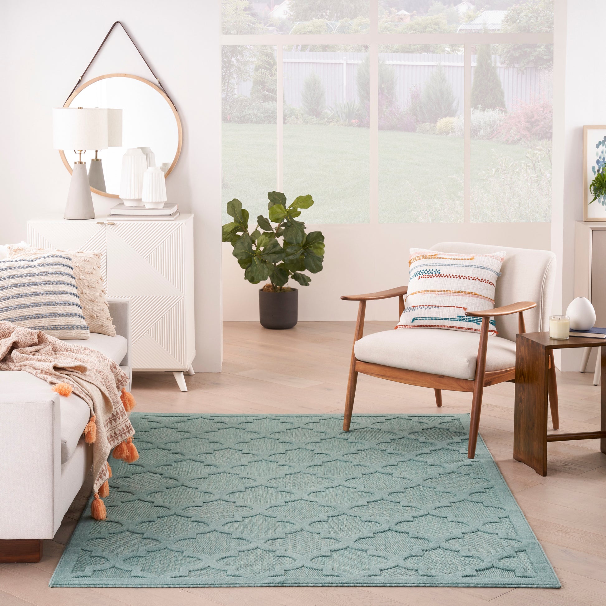 Teal geometric area rug anchors a bright Scandinavian living room with white sofa, wooden chair, plant, and round mirror.
