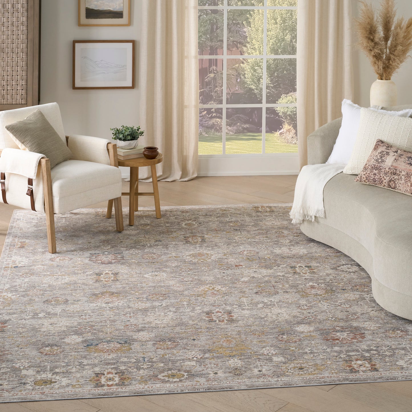 Cozy living room with a muted gray-beige rug, cream sofa, white chairs, wooden side table, and sunny window.