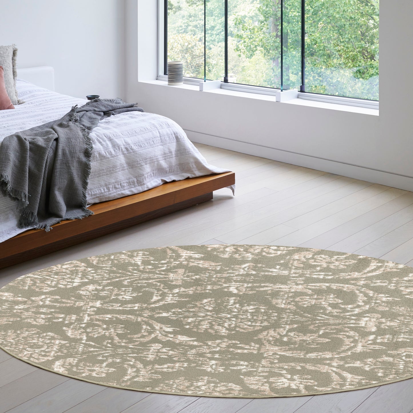 Beige circular rug with a subtle white abstract pattern in a bright minimalist bedroom with a low wooden platform bed.