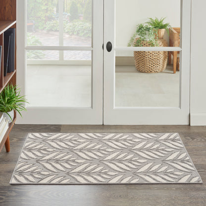 Rectangular gray and ivory leaf-patterned entry rug on a wood floor in front of glass French doors.