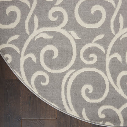 Round gray rug with a white scroll pattern and bound edge on dark wooden floor.