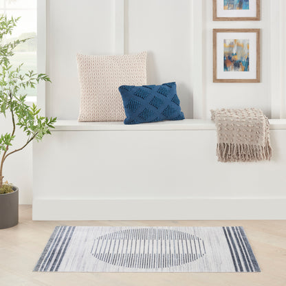 Blue striped mid-century modern rug 2' x 4' beneath a white built-in bench with beige knit cushion, blue lattice cushion, beige fringe throw, and a potted plant.