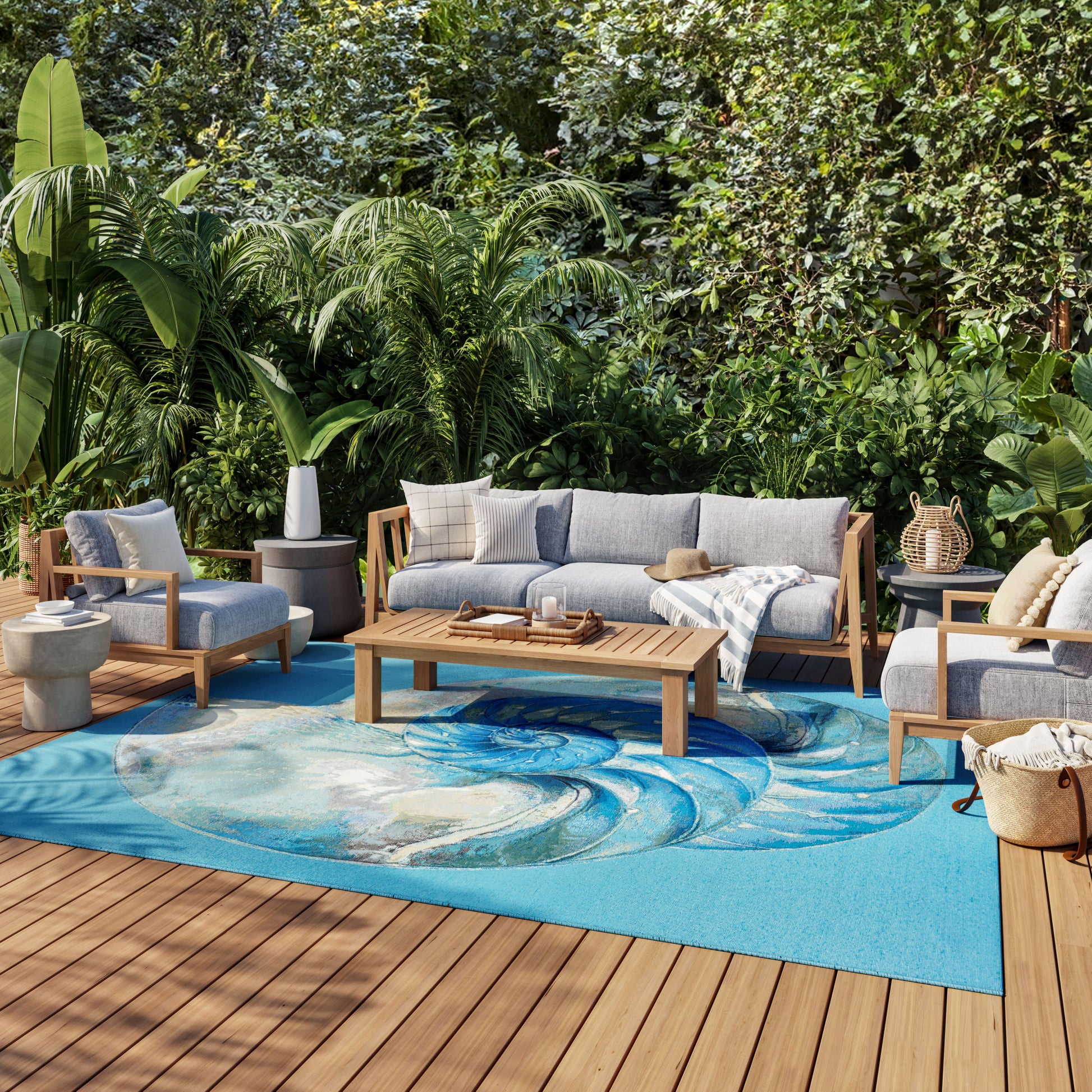 Outdoor wood-framed sofa set with light gray cushions, central coffee table on a bright blue swirl rug amid tropical plants.