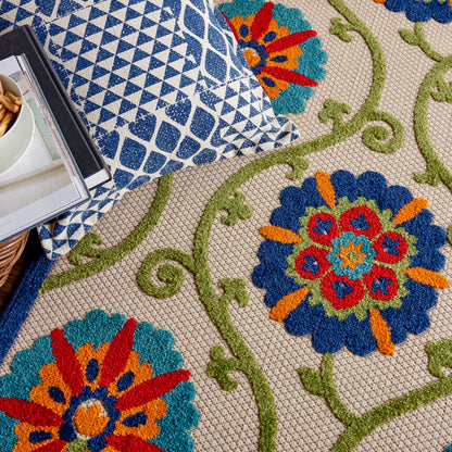 Colorful floral area rug with blue, teal, orange flowers & green vines; folded blue geometric textile on top.