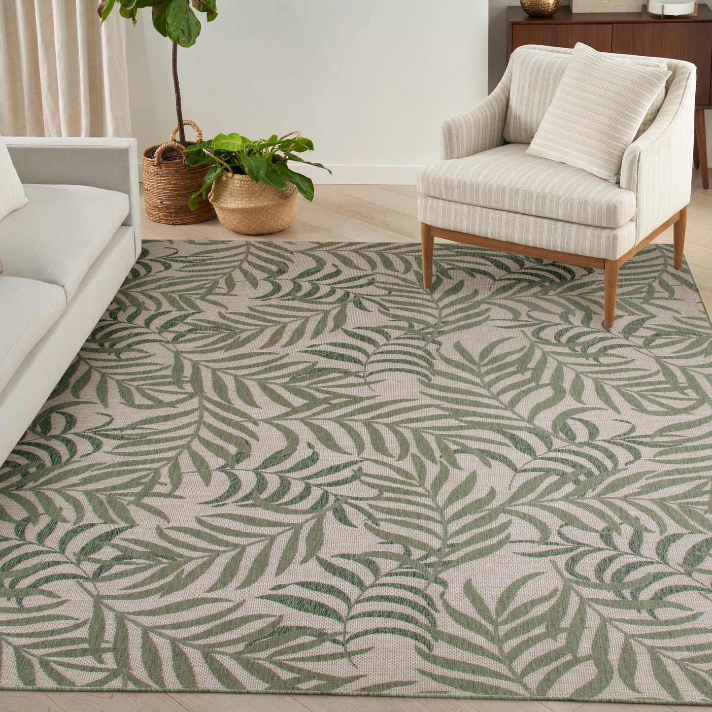 Beige area rug with green palm leaf pattern in a modern living room, paired with a cream sofa and striped armchair.
