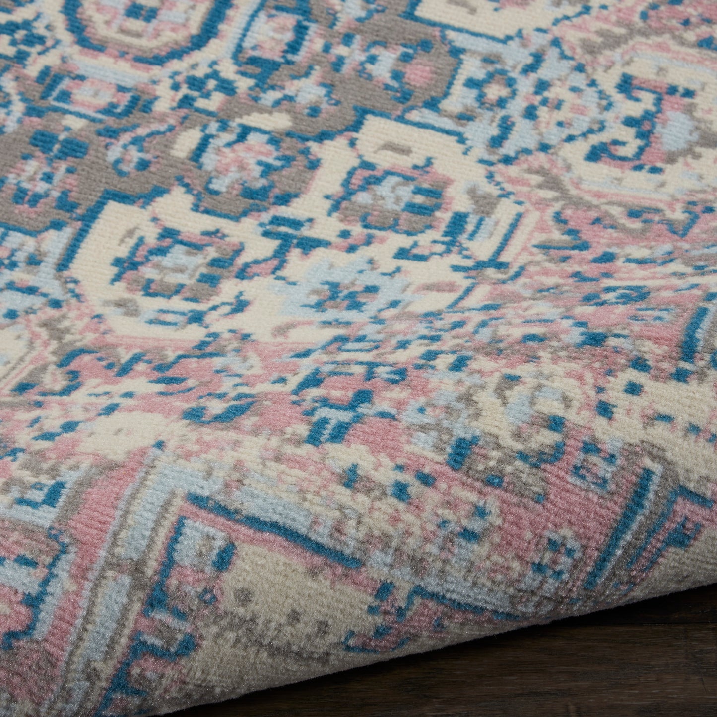 Distressed oriental rug with blue, pink and beige geometric medallions; medium-pile woven rug on dark wood floor