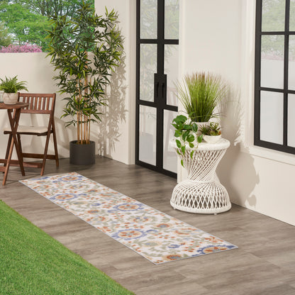 Beige runner rug with blue and orange floral medallions on gray wood floor beside potted greenery and white wicker planter.