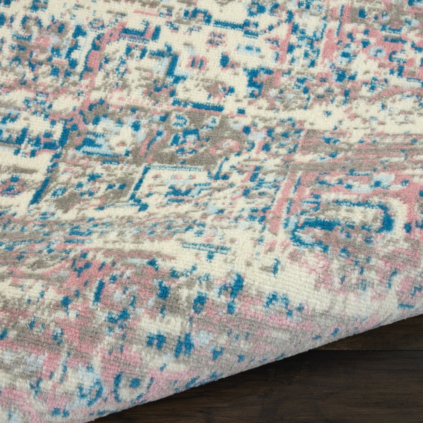 Pastel patterned area rug with pink, blue and gray geometric motif on cream, laid on dark wood floor.