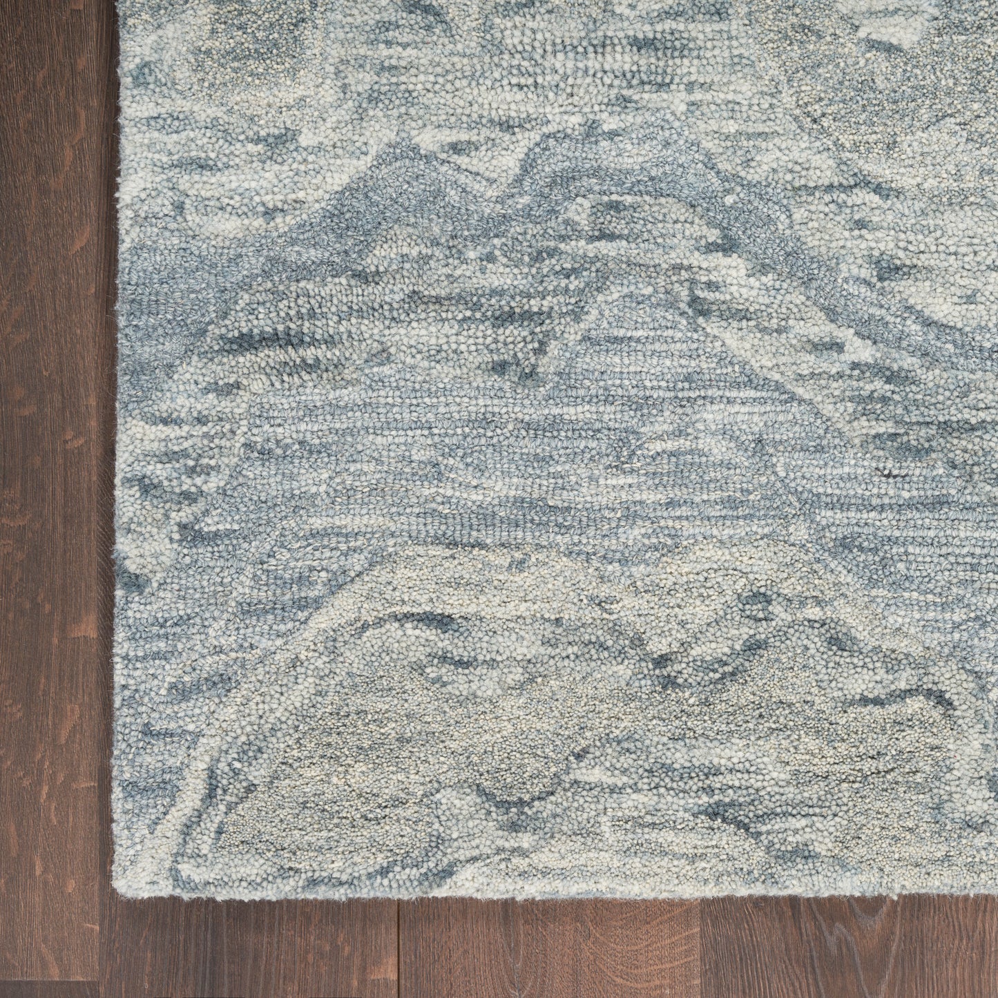 Blue-gray rug with a subtle mountain-like pattern and plush texture, finished edges on a dark wood floor.