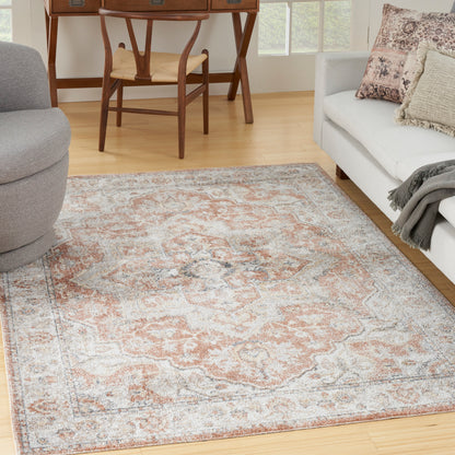 Peach, ivory & gray oriental-style area rug on light wood floor with a gray sofa & wooden desk in back.