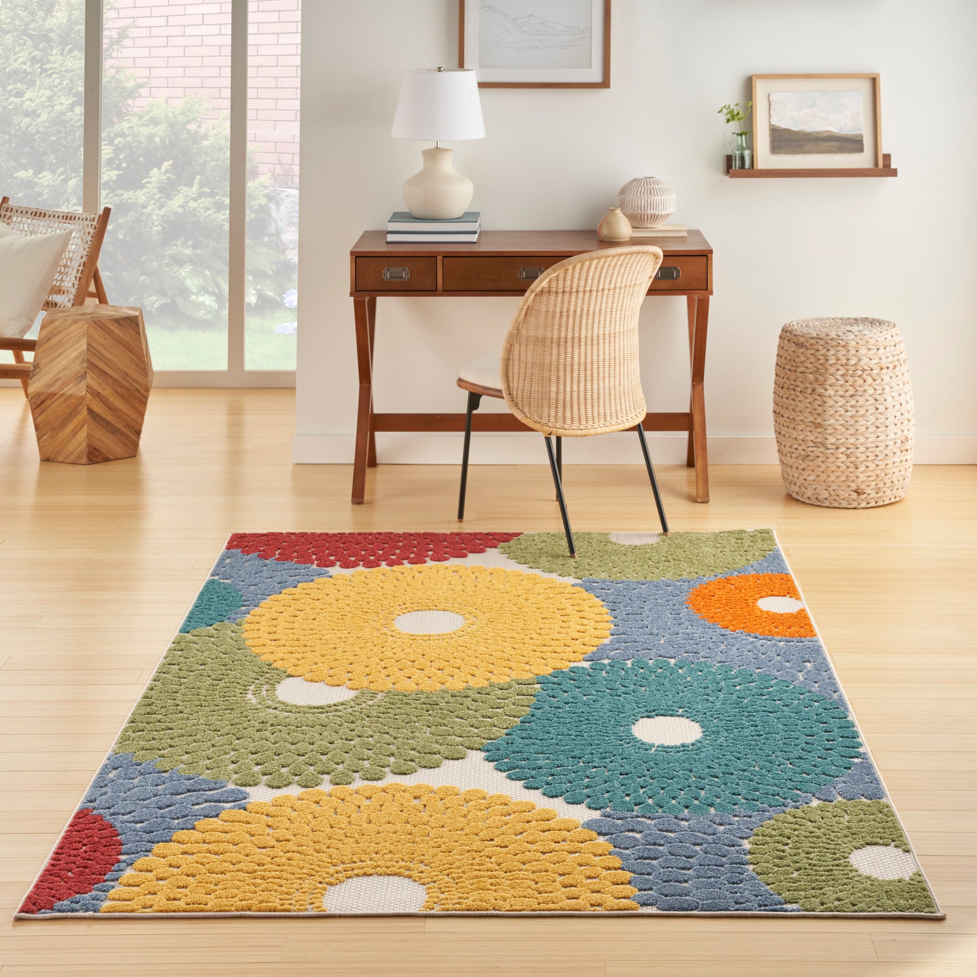 Colorful circular-pattern rug in yellow, teal, green and orange under a wooden desk with a wicker chair.