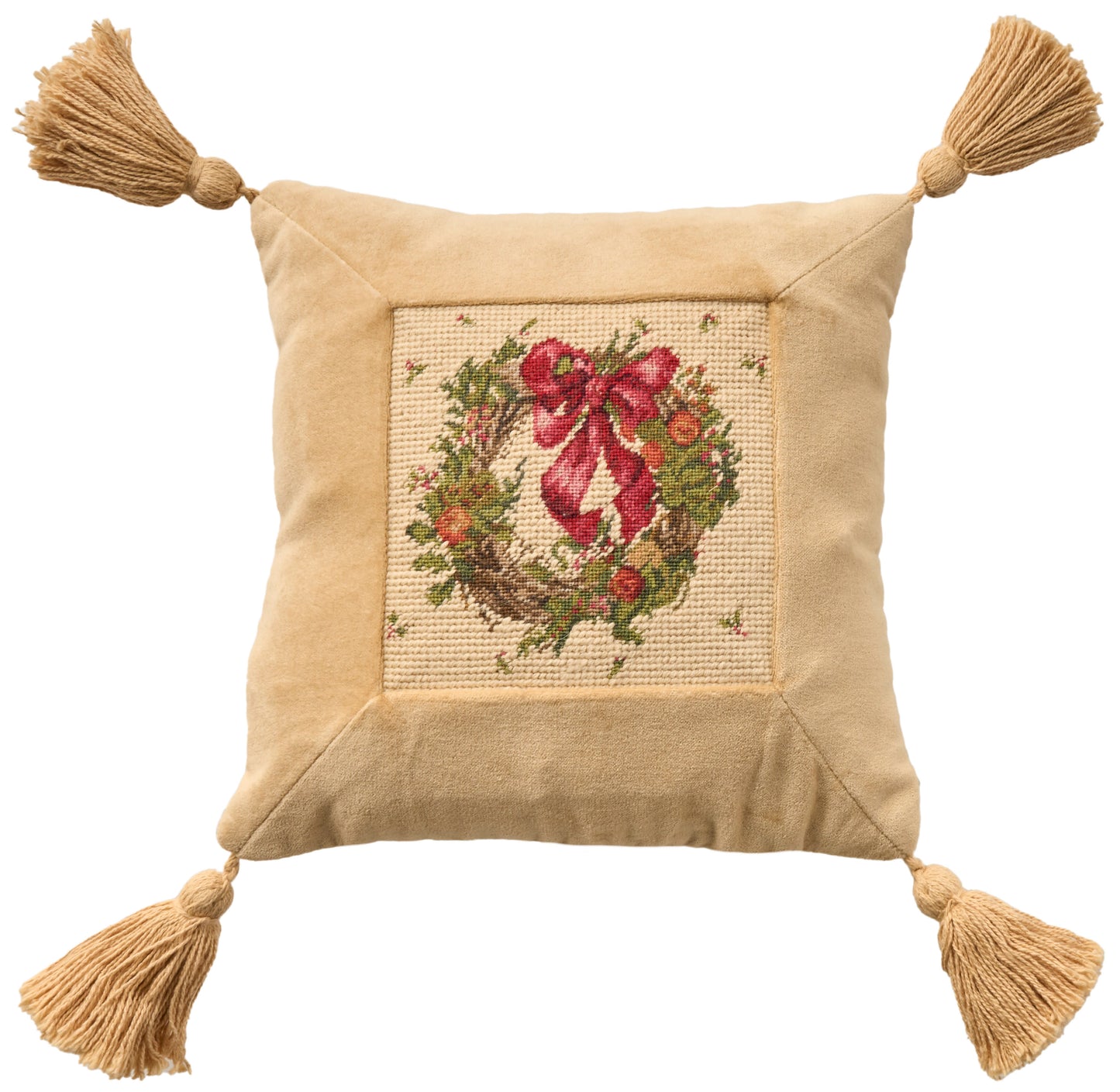 Beige square throw pillow with cross-stitched wreath and red bow, tassels at all four corners.