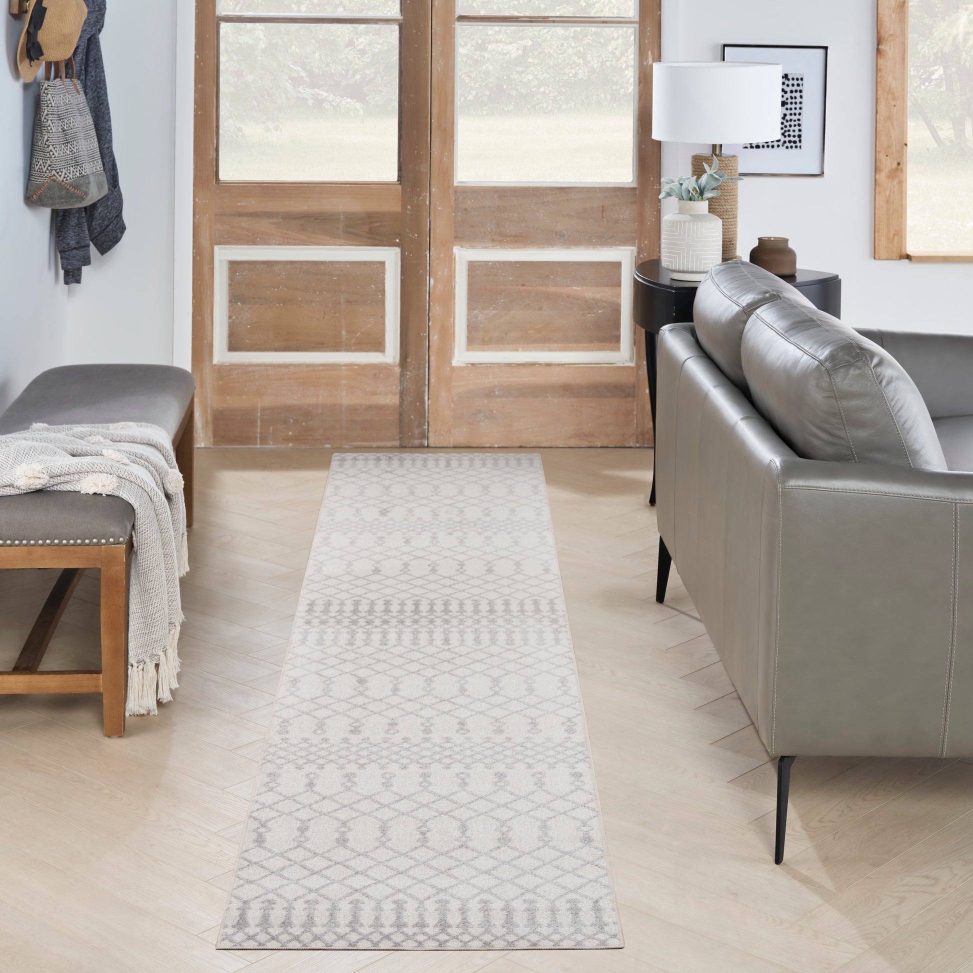 Woven light gray geometric runner rug in a modern living room with a gray sofa, bench and wooden double doors in back.