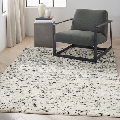 Modern gray fabric armchair with black steel frame beside a concrete-gray side table; cream and black abstract rug.