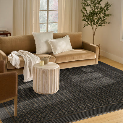 Beige fabric sofa with white fringe pillows, cream throw, round ribbed wood table, dark rug, potted tree.