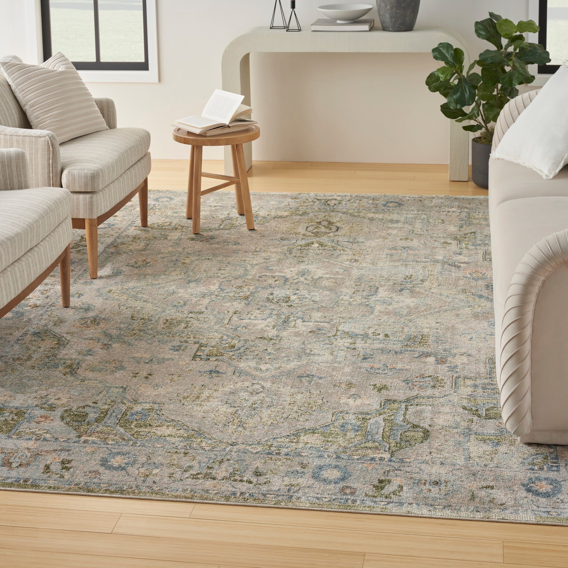 Muted blue-gray oriental rug with beige and green motifs in a bright living room with cream seating and wood furniture.