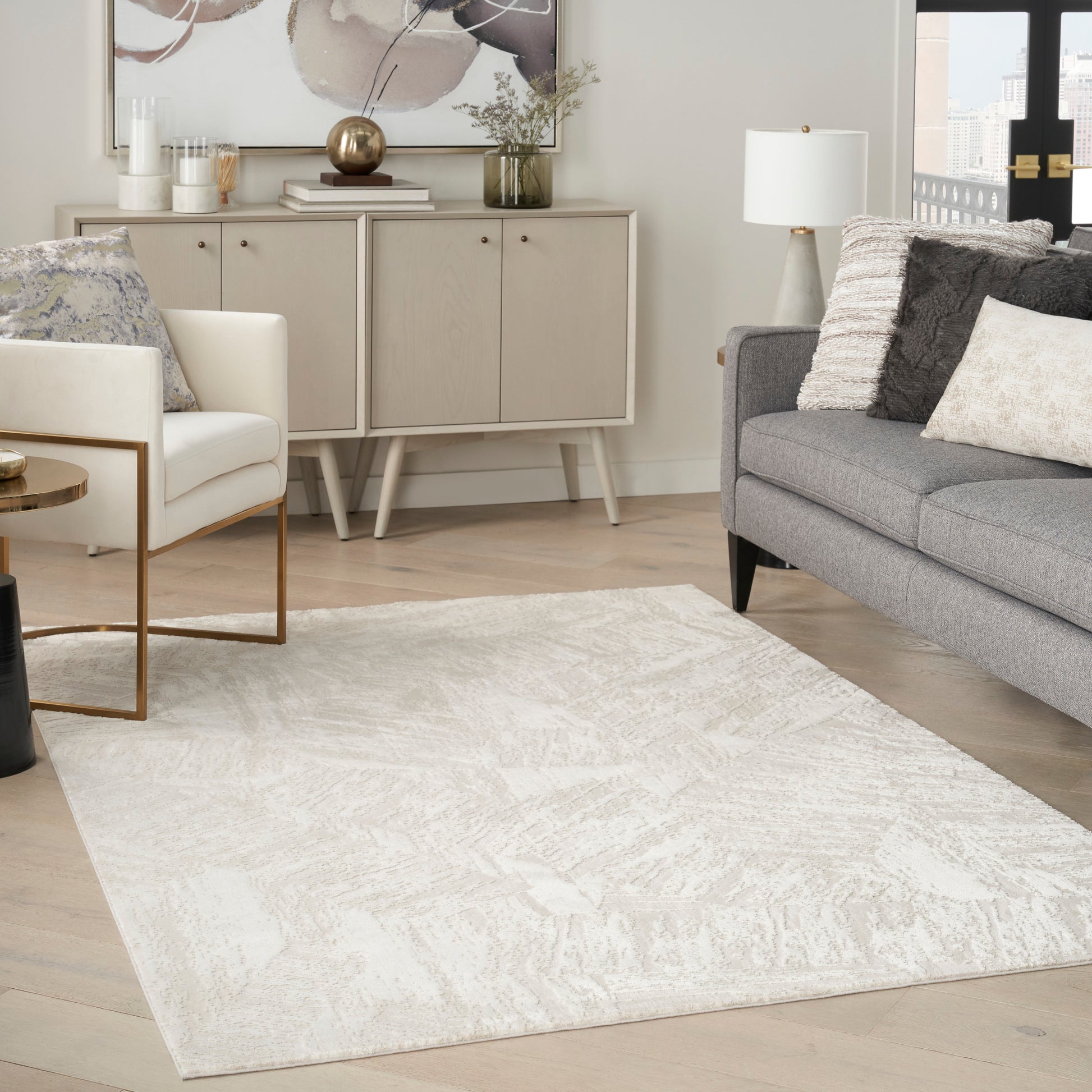 Cream textured area rug with a subtle abstract pattern in a modern neutral living room with a gray sofa and white accent chair.