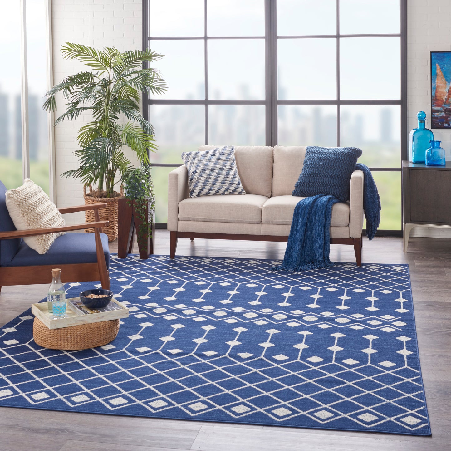 Cozy living room with a blue and white geometric area rug, beige sofa with navy throw, wooden chair, plant, and blue accents.