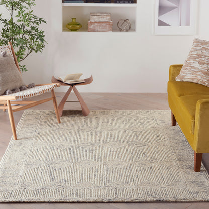 Cozy living room with beige geometric 4' x 6' rug, mustard sofa, woven wood chair, small curved coffee table, open book.