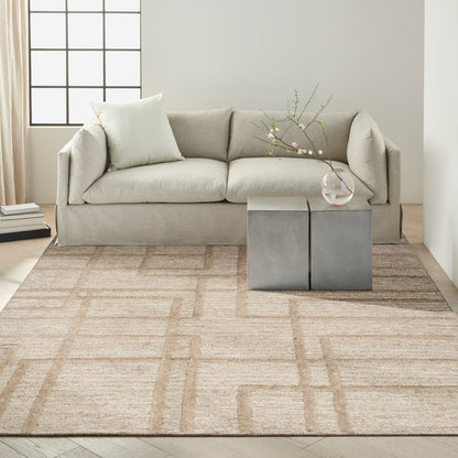 Neutral living room with light gray sofa, beige geometric rug, and gray block coffee table with a glass vase and branches.