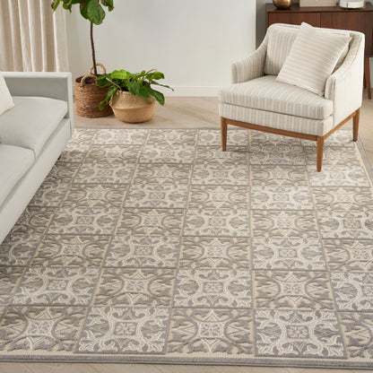 Neutral woven area rug with gray & cream square tile motif in a living room with beige sofa, striped armchair & plants.