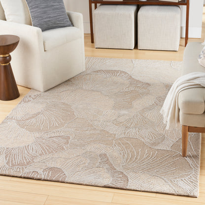 Rectangular beige area rug with large leaf motif on light wood floor, beside cream sofa and woven cube ottomans.