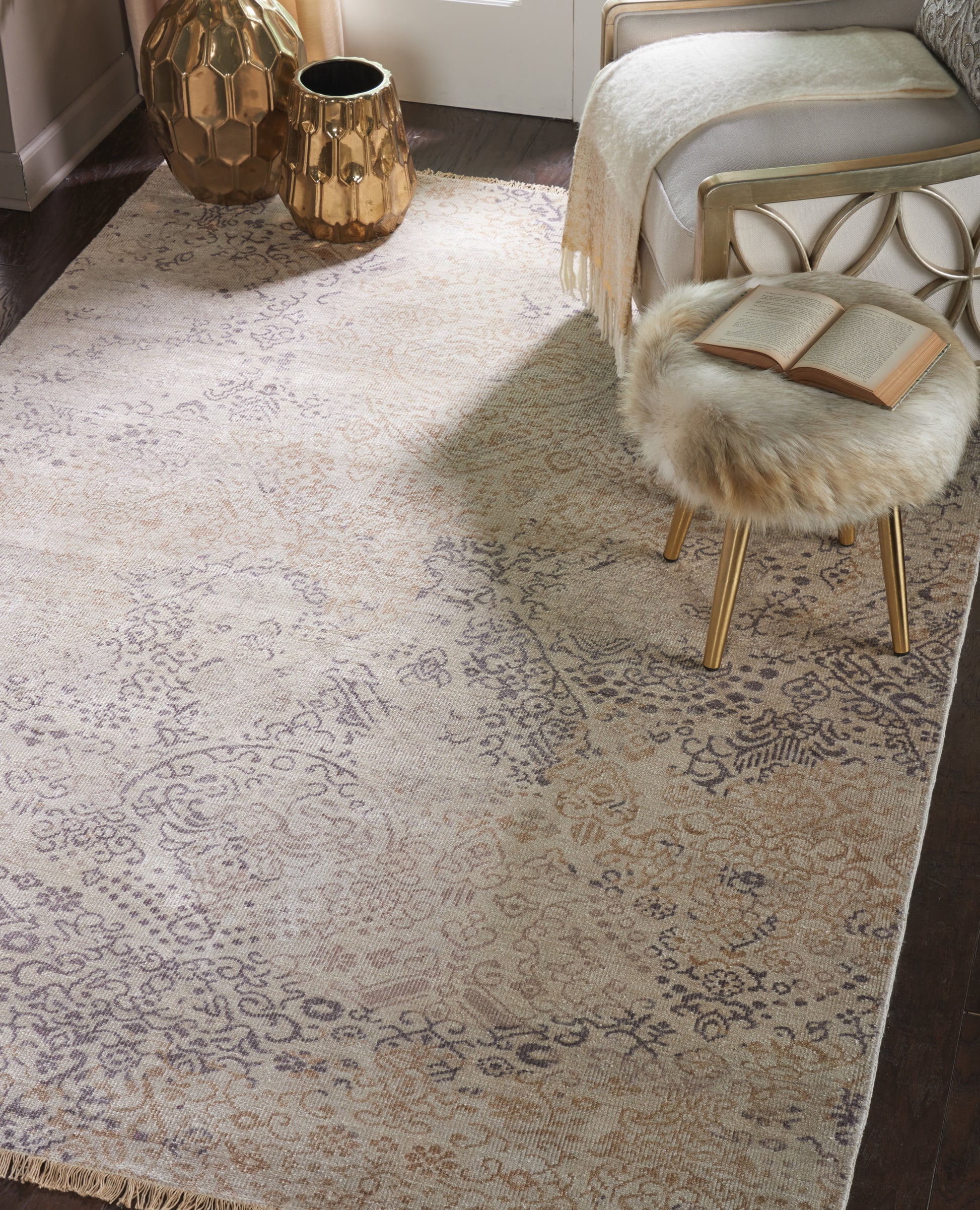 Cream ornate patterned area rug with taupe floral motifs; glam bedroom with gold metal bed frame, fur stool & gold vases.