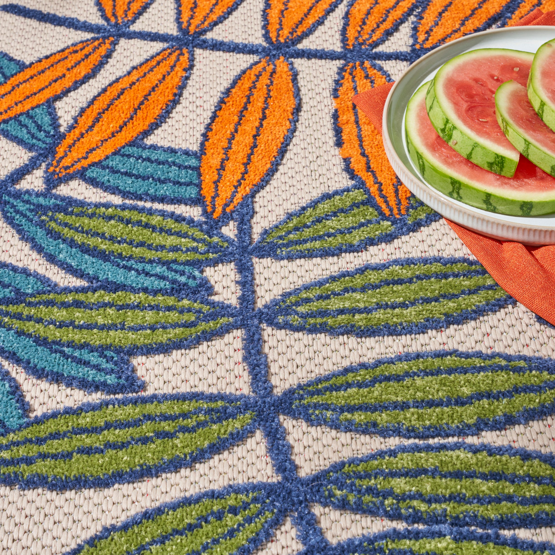 Colorful woven round rug with blue and green leaf pattern and orange accents