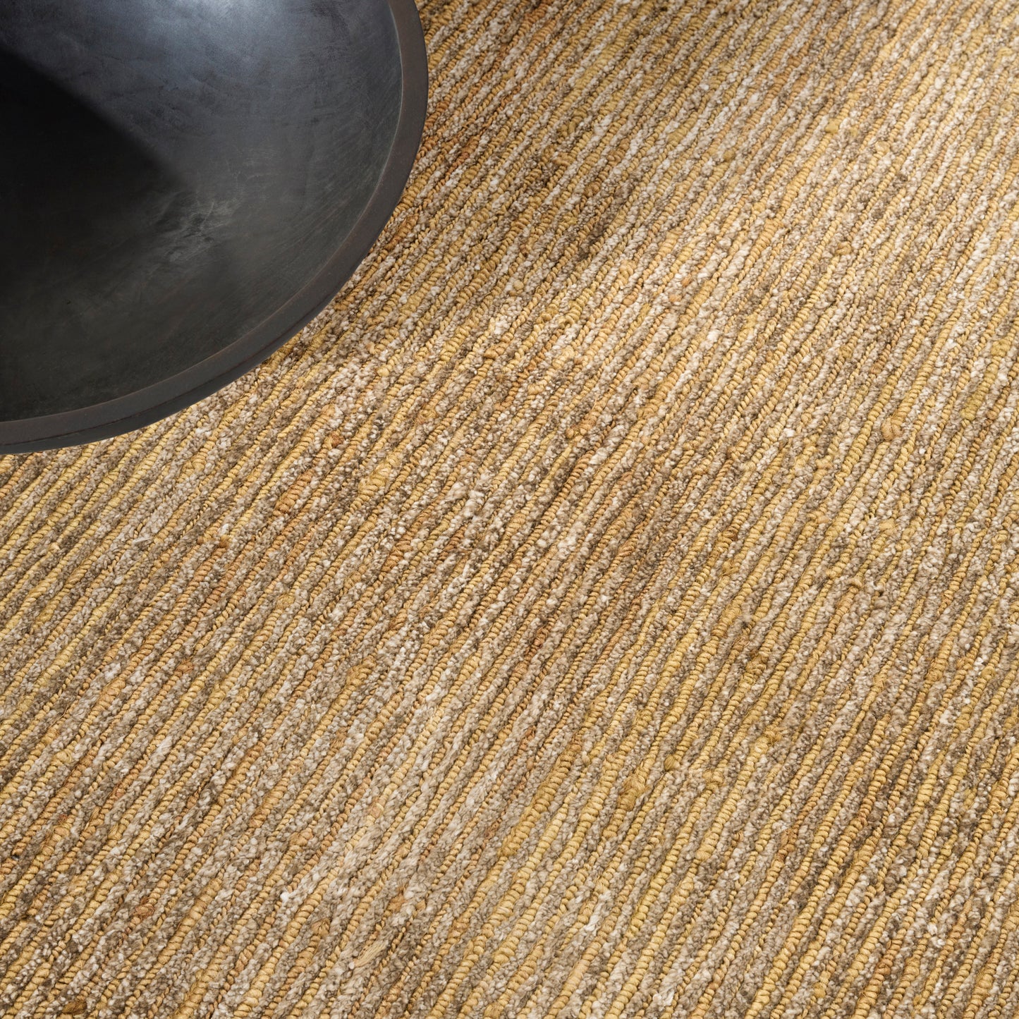 Partial view of a matte black ceramic bowl on a beige woven jute rug with striped texture.