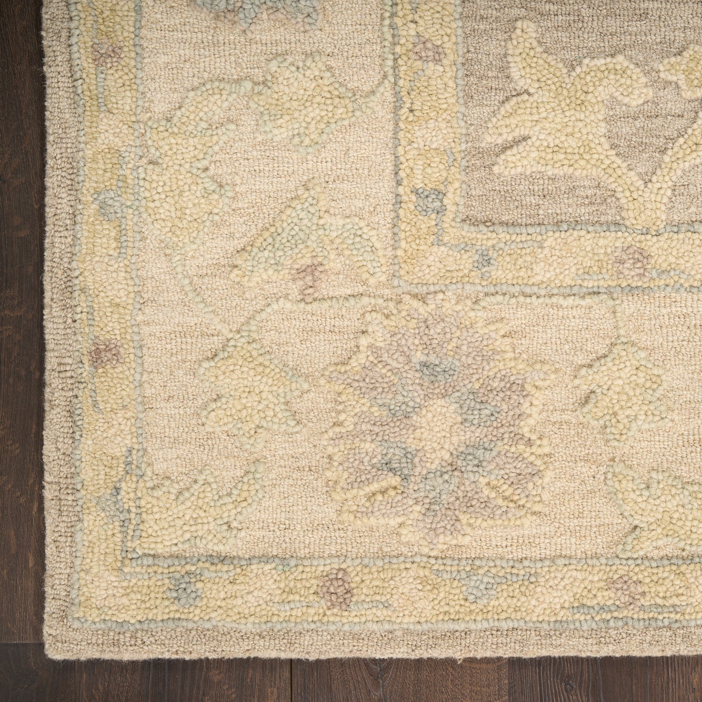 Beige oriental rug with pale yellow, blue, and gray floral medallions and a decorative border on dark wood floor.