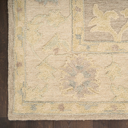 Beige oriental rug with pale yellow, blue, and gray floral medallions and a decorative border on dark wood floor.