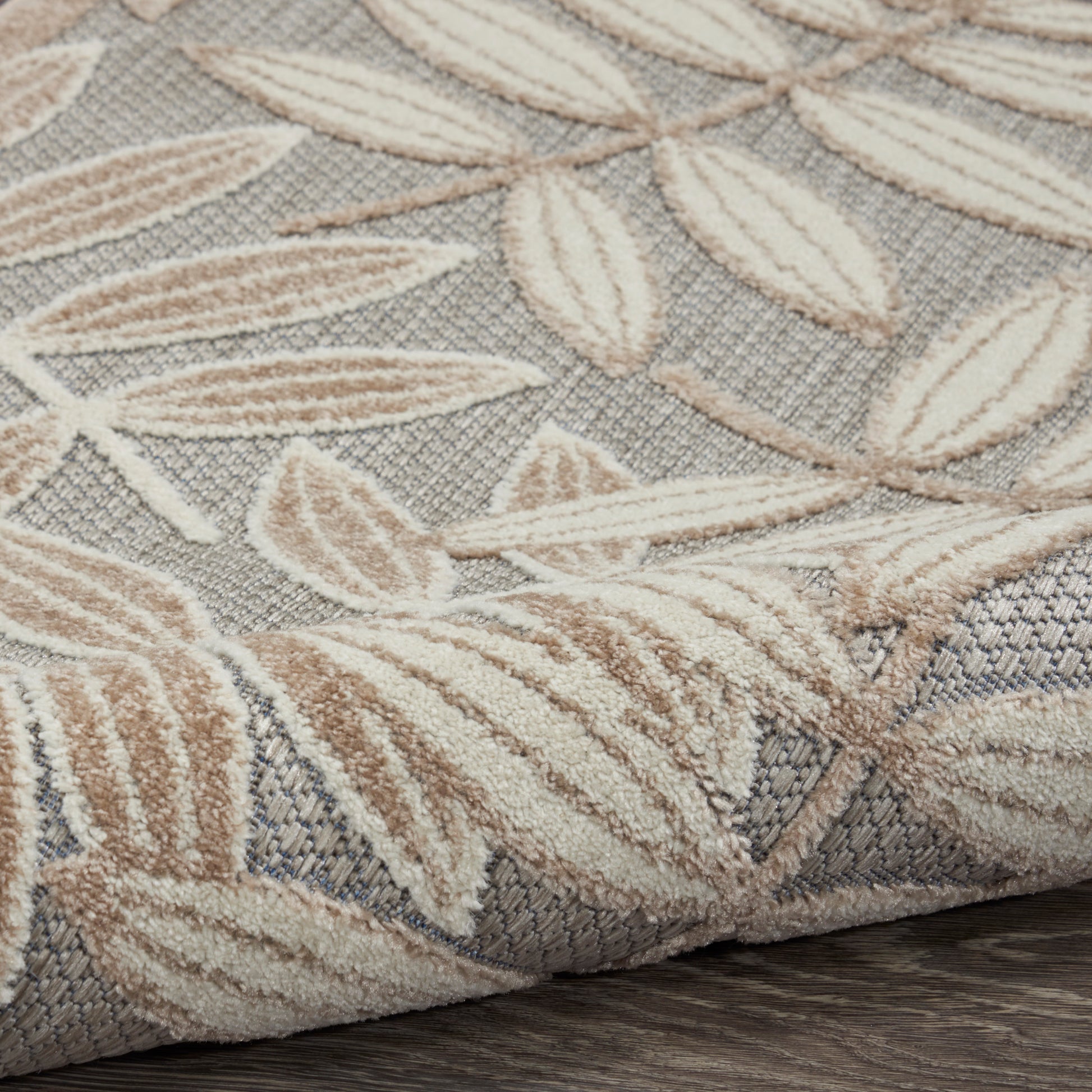 Beige leaf-patterned woven rug with textured pile & folded edge on dark wood floor.