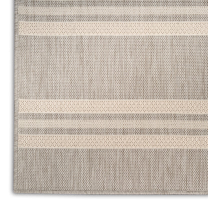 Neutral striped woven rug in beige and gray with dotted accent bands; rectangular, casual living room underfoot.