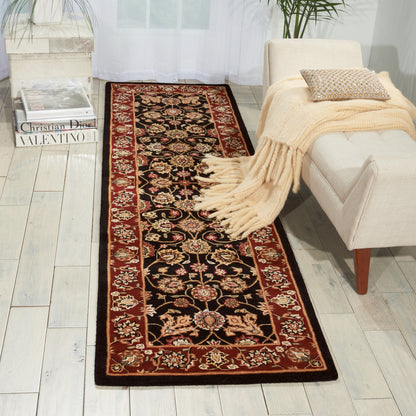 Long oriental runner with black field, red border & floral motif on light wooden floor beside a cream sofa with a beige throw.