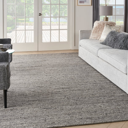 Living room with grey sofa, rug, French doors, beige and grey cushions, and a grey armchair with a glass side table.