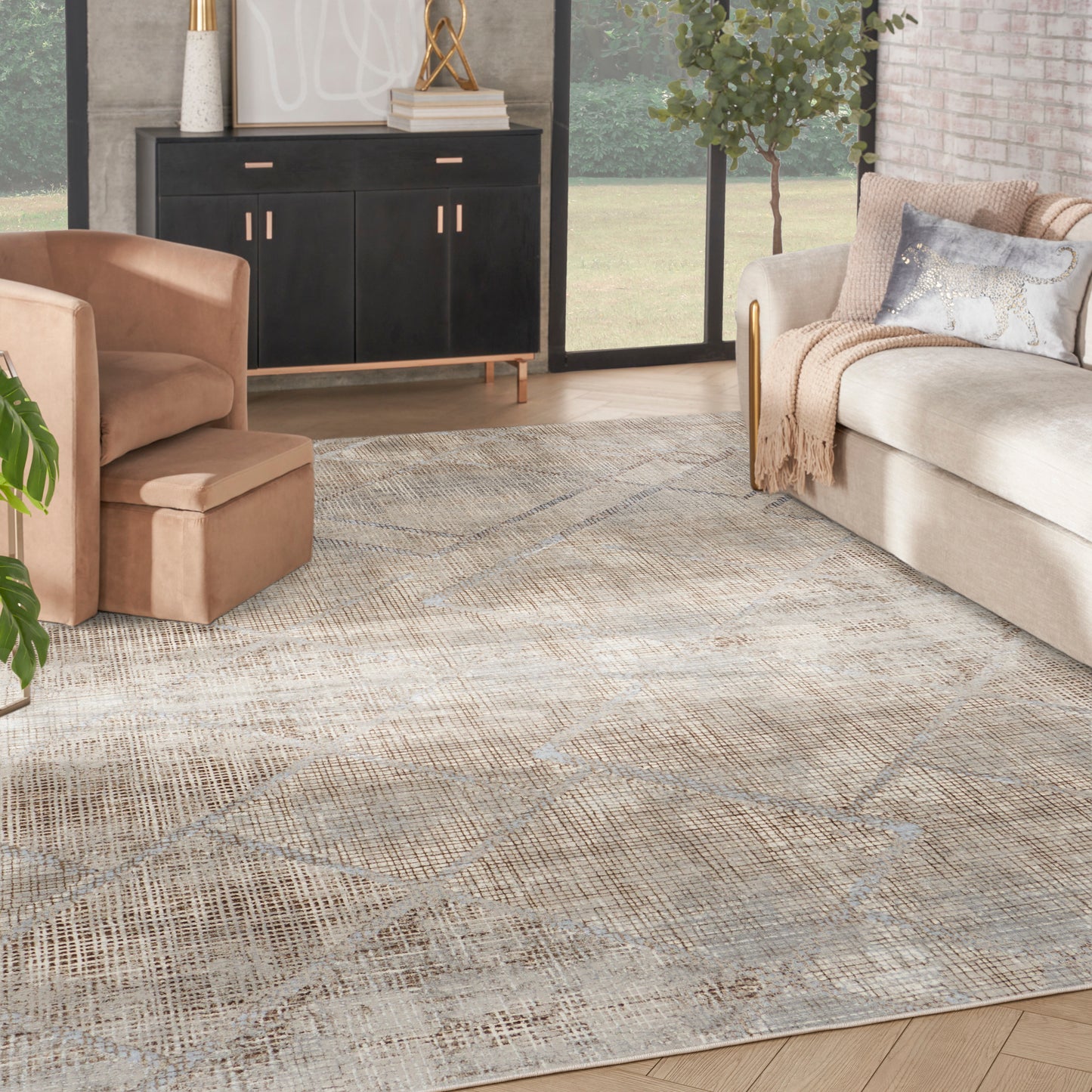 Neutral modern living room with a textured beige area rug, cream sofa, tan armchair, & black gold-accent sideboard.