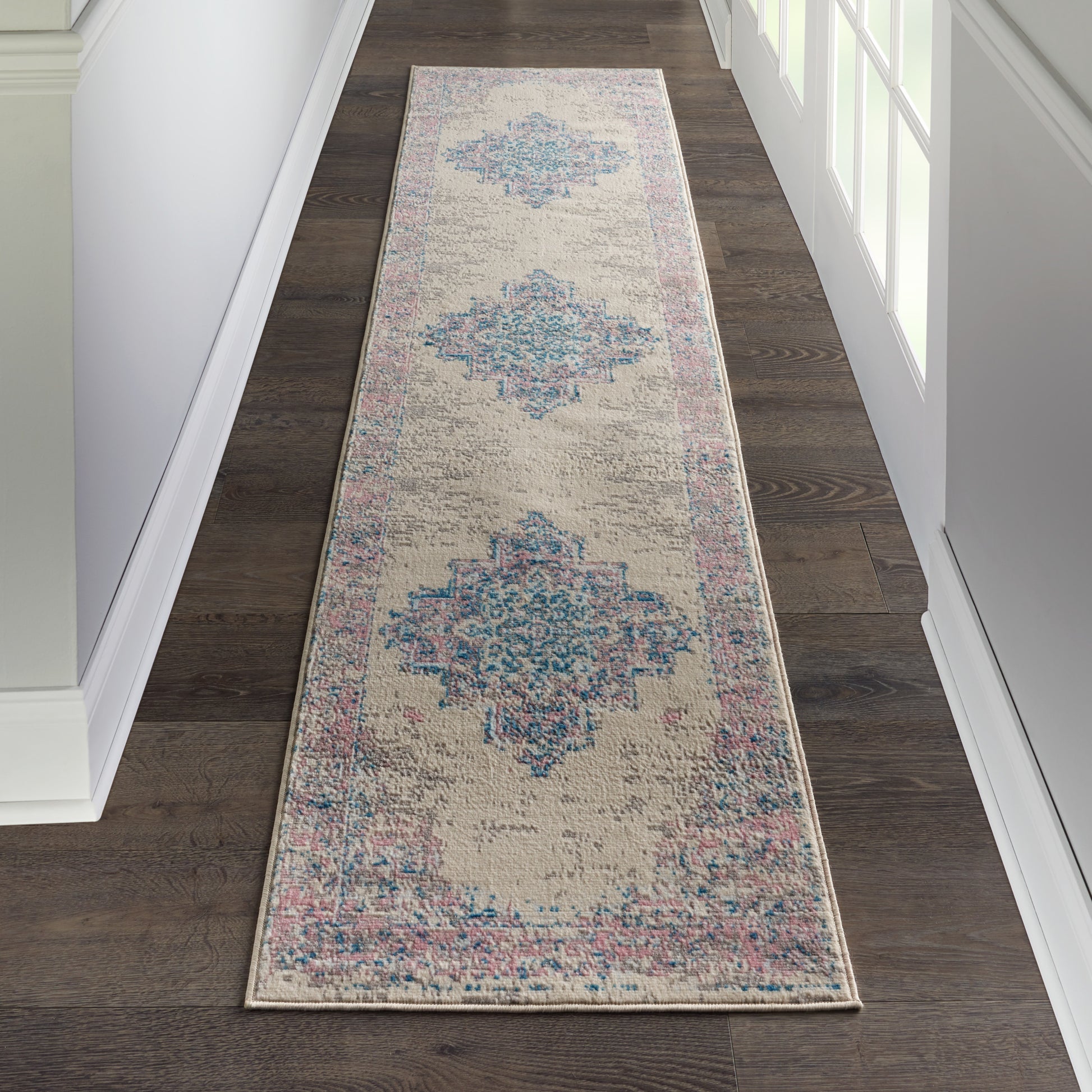 Distressed beige hallway runner rug with blue diamond medallions and pink border on dark wood floor.