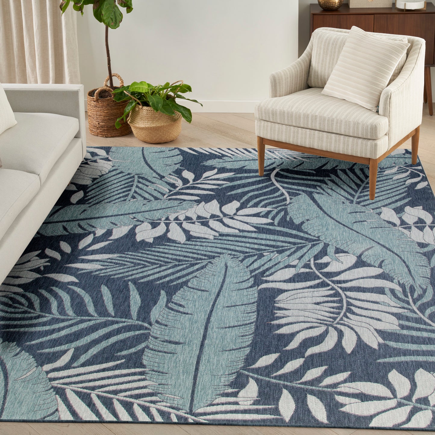 Blue tropical leaf rug with navy and teal tones under a cream sofa and beige armchair in a bright living room.