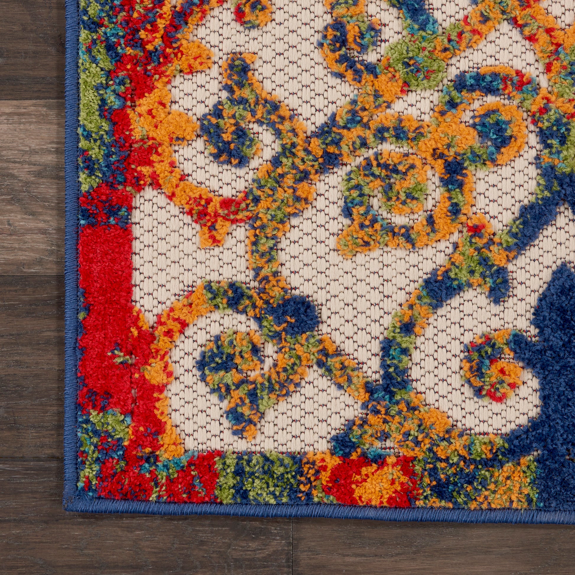 Close-up of a vibrant Persian-style rug with blue border and fringed edge, multicolor floral-scroll pattern on ivory lattice.