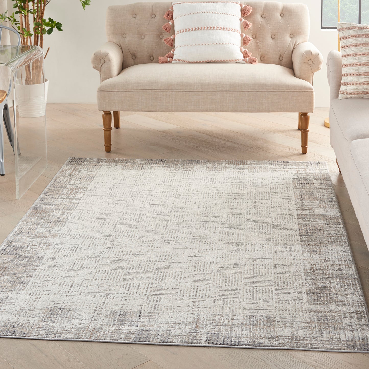 Cozy neutral living room with a beige tufted sofa, light-wood legs, and a large textured grey area rug.