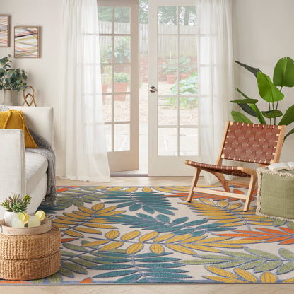 Bright living room with French doors, sheer curtains, a tropical leaf rug, wicker ottoman, woven chair, and potted plants.