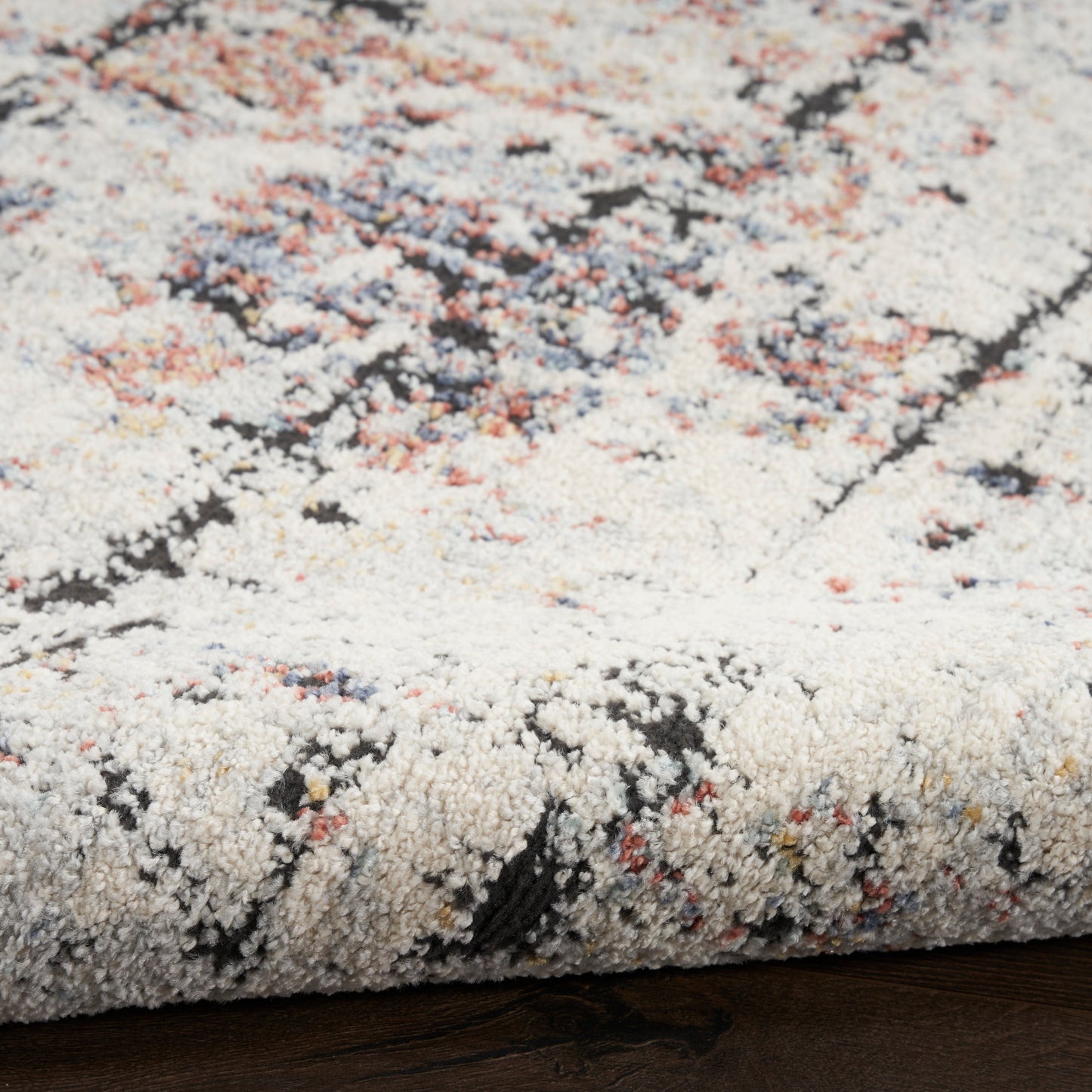Cream textured rug with abstract multicolor pattern (pink, blue, orange, black); plush cut-pile and rolled edge.