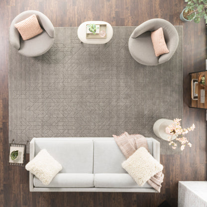 Top-down living room with light gray sofa, cream pillows and blush throw, two round gray chairs, and a gray geometric rug on dark wood floor.
