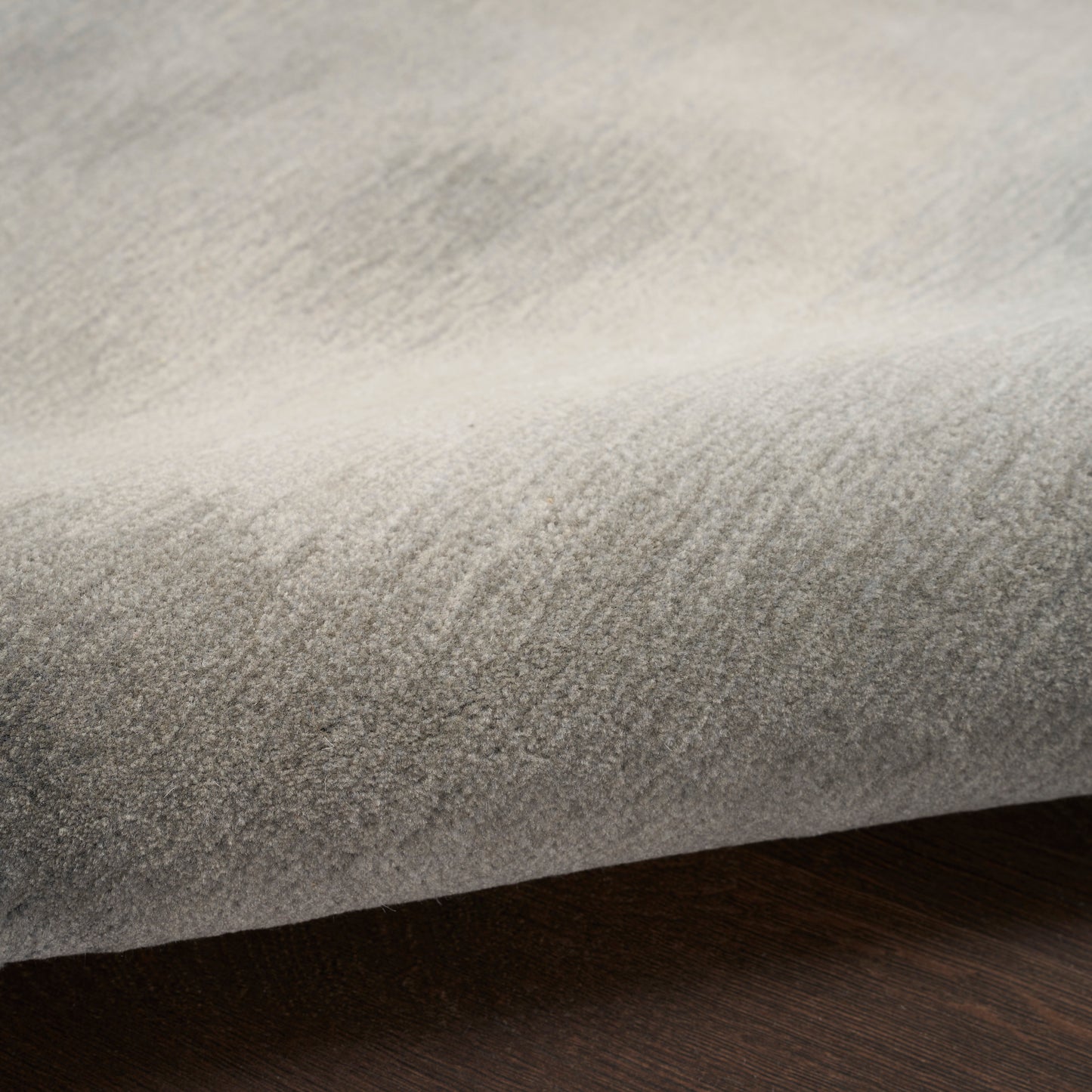 Folded light gray velvet-like rug with subtle nap on dark wood surface.