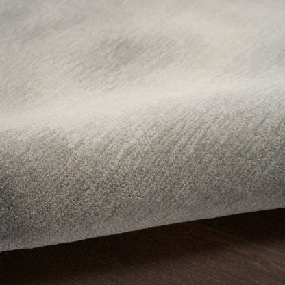 Folded light gray velvet-like rug with subtle nap on dark wood surface.