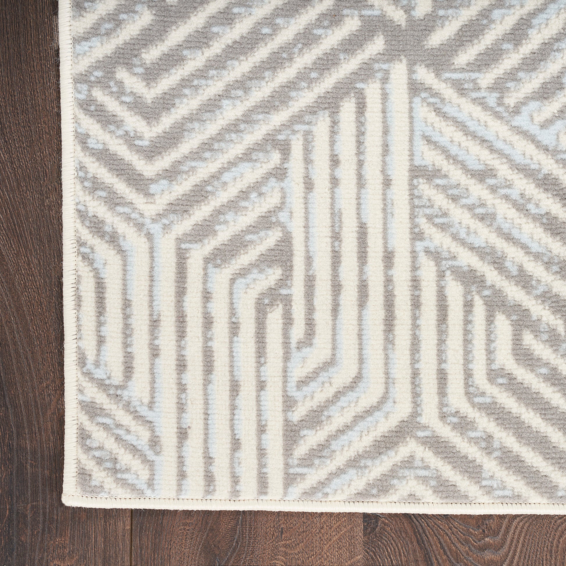 Rectangular woven rug with light gray and ivory geometric maze pattern on a dark wood floor.