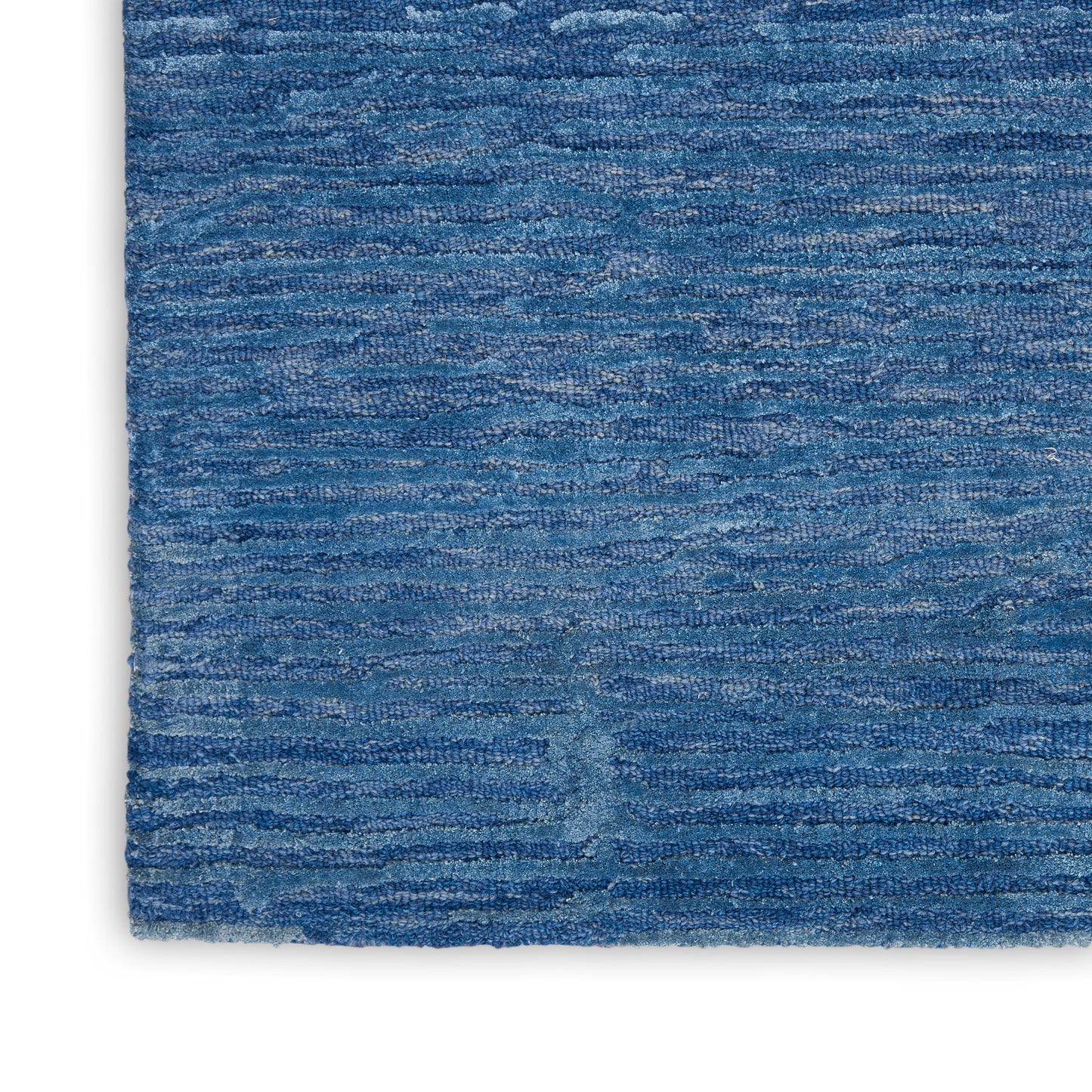 Blue textured rug close-up with variegated denim blues and subtle horizontal stripes, plush pile.