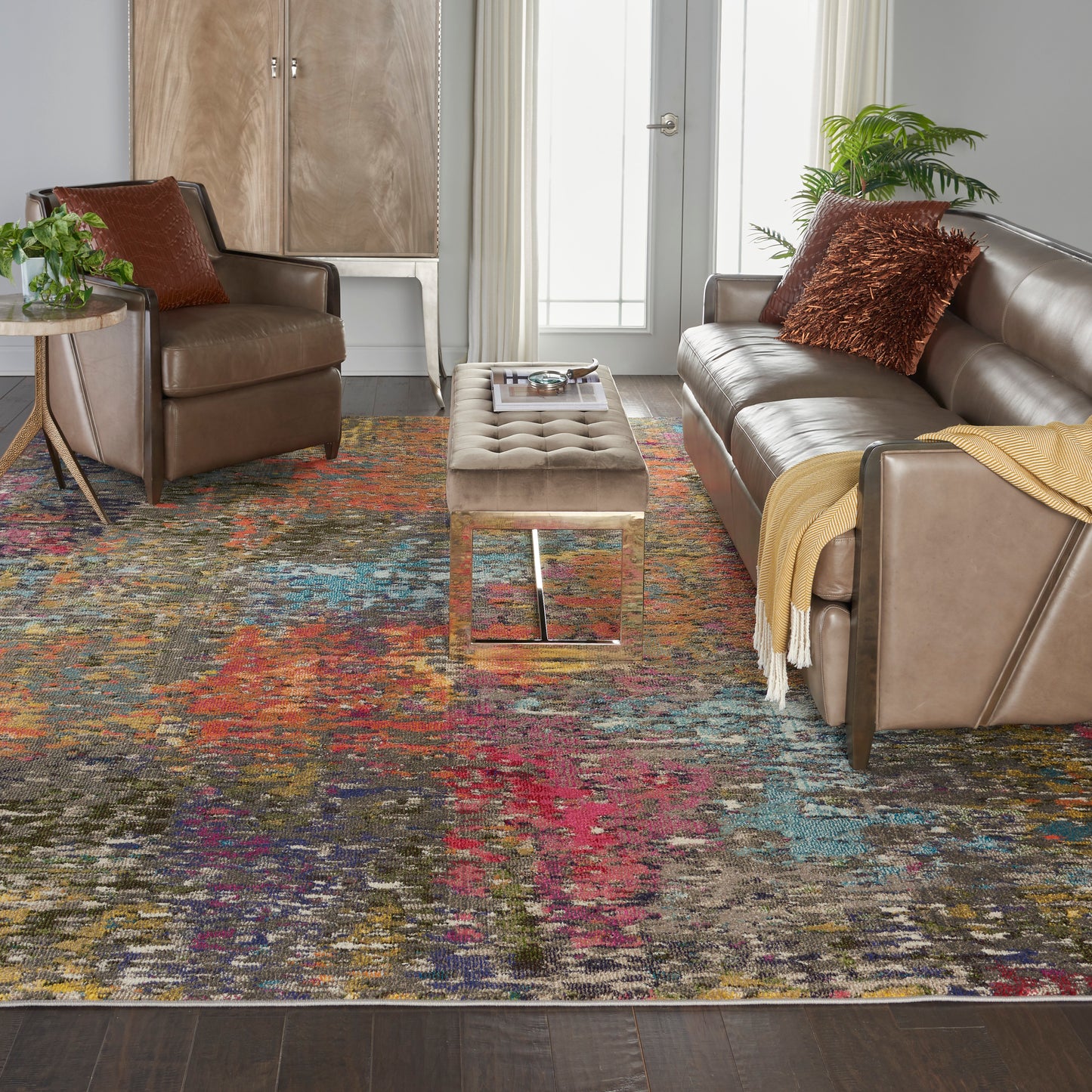 Cozy contemporary living room with brown leather sofa and armchairs, tufted beige ottoman, and a vibrant multicolor rug.
